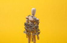 Wooden Puppet Wrapped In Steel Chain On Yellow Background