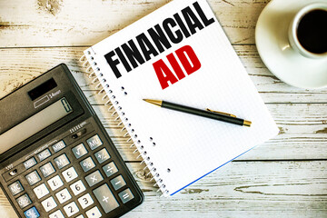 FINANCIAL AID written on white paper near coffee and calculator on a light wooden table. Business concept