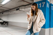 © Andrii  - Fashionable girl with mobile phone in underground parking. Woman is texting online