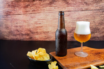 Poster - A glass and bottle of cold beer and a bowl of crunchy chips served on a wooden board