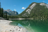 Fototapeta Na drzwi - A panoramic view on the Pragser Wildsee, a lake in South Tyrolean Dolomites. High mountain chains around the lake. The sky and mountains are reflecting in the lake. Dense forest at the shore. Serenity