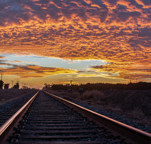 Train Tracks Of The Rural Railraod Converge Off In The Distance Where The Horizon Meets The Vibrant Colored Clouds In The Sky.