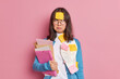 © wayhome.studio - Frustrated female manager has remote work poses with paper documents checks information and prepares research work wears round spectacles sticker stuck on forehead isolated over pink background