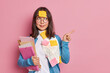 Horizontal shot of brunette Asian woman manager examines paper documents points away on blank space works on startup project isolated over pink background. Check this out. Education and studying
