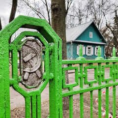 USSR national emblem on old metal fence  with wooden house in the back