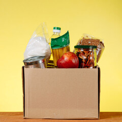 Wall Mural - Donation Box With food For Donation On Yellow Backround. Assistance To The Elderly In The Context of The Coronavirus Pandemic. square image