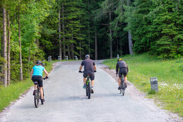 Three unrecognizable tourists bike up an empty asphalt road near Kranjska Gora.