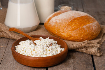 Glass jar of milk, bowl of cottage cheese and bread on wooden table