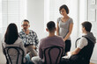 © Photographee.eu - Middle age woman stands in front of a group of people during a therapy meeting and talks about her family problems