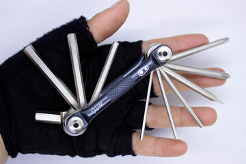 Hand wearing cycling glove holding a multi tool allen set or hex set used for bicycle repair closeup, white background and top view.space for text.
