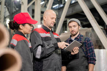 Poster - Serious bald mature foreman pointing at tablet display while making presentation