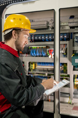 Poster - Young engineer in workwear and hardhat pointing at electronic sketch or scheme