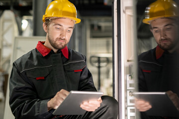 Poster - Young serious engineer in workwear and hardhat scrolling through technical data