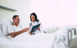 © My Ocean studio - Handsome mature patient man is lying on the clinic bed and has a conversation with a confident young woman doctor in a white coat