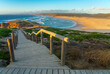Wooden walkway with panoramic view of a large beach on the ocean at sunset