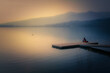 Persona seduta su un pontile che guarda al lago con montagne al tramonto 