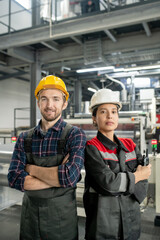 Poster - Two young workers in helmets and workwear standing against interior of workshop