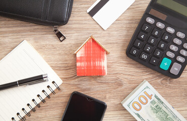 Wall Mural - Wooden house model with a wallet, credit card, calculator, money, smartphone, pen and notepad.