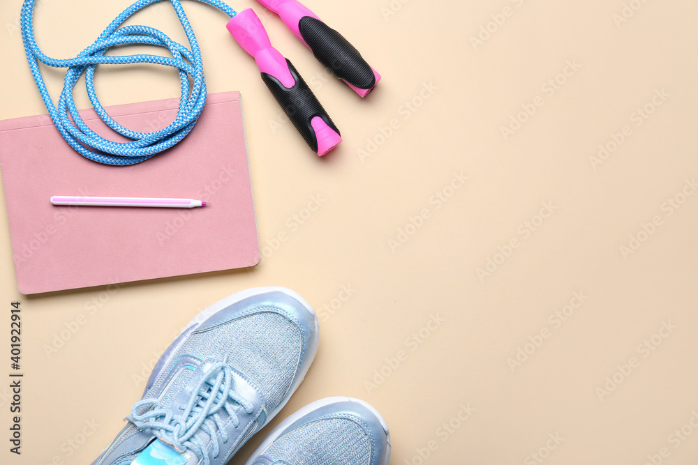 Sportive shoes, jumping rope and notebook on light background