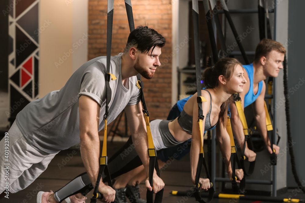 Sporty people exercising with TRX straps in gym
