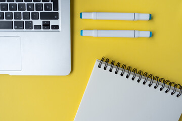 Wall Mural - A high-angle shot of a yellow desk with a laptop, pens, and a notebook