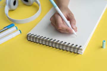 Wall Mural - A person's hand writing in a notebook next to headphones on a yellow desk