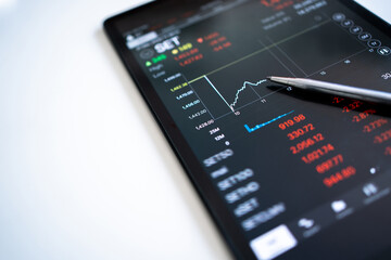 Poster - The pen points to the trader's selling price displayed as a graph falling on a tablet screen.