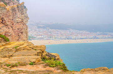 Wall Mural - Top view of rocks and cliffs, azure turquoise water of Atlantic Ocean and sandy beach coastline Praia da Nazare town background, Leiria District, Oeste region, Portugal