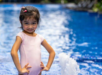 Portrait of pretty asian child smilling and posing on swimming pool background wearing pink swim suit