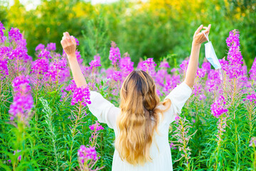 The girl who removed the medical mask from her face raised her hands up in a gesture of joy on a green summer background. End of quarantine concept