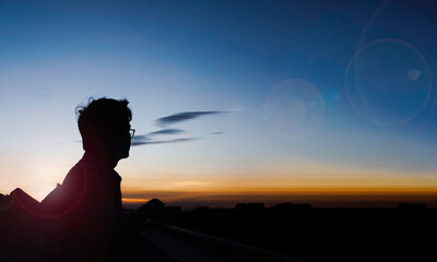 Wall Mural - a silhouette of a person looking at a sunset. The sky is a mix of orange, yellow, and blue.