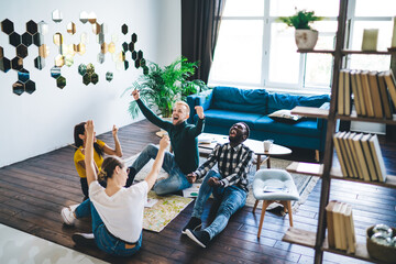 Wall Mural - Excited multiracial friends sitting on floor in light apartment