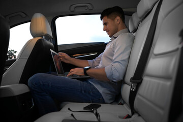 Wall Mural - Handsome man working with laptop on backseat of modern car