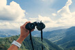 Hands holding binoculars on mountains forest nature background, looking through binoculars, travel, search and search concept.