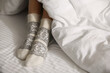 © New Africa - Woman wearing knitted socks under blanket in bed, closeup