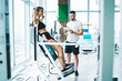 © BullRun - Instructor with tablet near sportswoman exercising on modern gym equipment