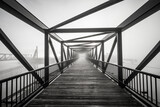 A grayscale shot of light at the end of a modern beautifully architectured bridge surrounded by fog