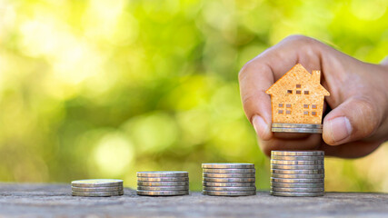 Wooden house model on coins and people's hands, real estate investment ideas and financial transactions.