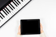 Top view to kid hands holding tablet computer. Digital piano at white desk. Online learning, remote education