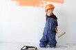 © Andrii Lysenko - a little boy wears an orange hard hat on his head and a large jumpsuit raises his thumb up. Copy space.
