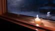 Candle sitting on a window sill. Candle light glowing in the dark at night background. Christmas Christ candle decoration warmth in the cold winter season