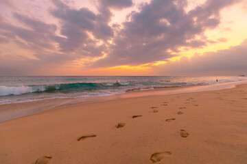 Wall Mural - Beautiful ocean sandy beach under sunset sky with footprints in a sand.