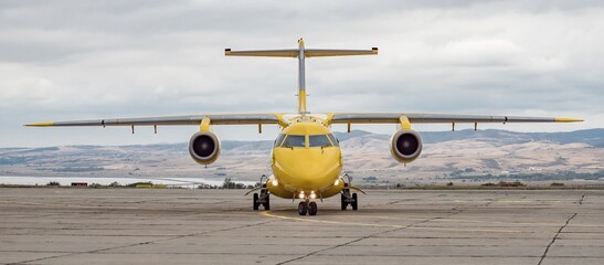 Wall Mural - Front view of yellow airplane. Jet aircraft taxiing on airport apron, dynamic dark grey cloudy sky background. Modern technology in fast transportation, private business travel, charter flight.