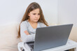 © QKon Studio - Emotional portrait of attractive cute girl 6-7 old she is tired in a bad mood sitting using laptop on distance learning