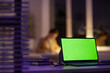 © Seventyfour - Modern office workplace late in evening with green screen laptop on foreground and unrecognizable woman working on background, copy space