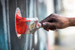 A closeup shot of a graffiti artist's hand dirty in paint holding a paintbrush and painting on a wall