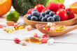A selective focus shot of fresh fruits and vegetables with different medicine on a wooden spoon