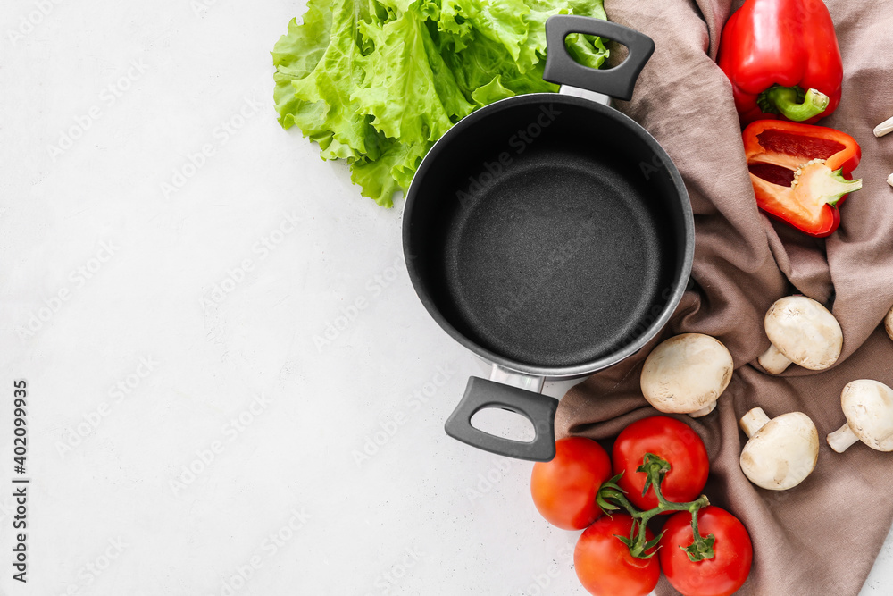 Cooking pot with vegetables and mushrooms on light background