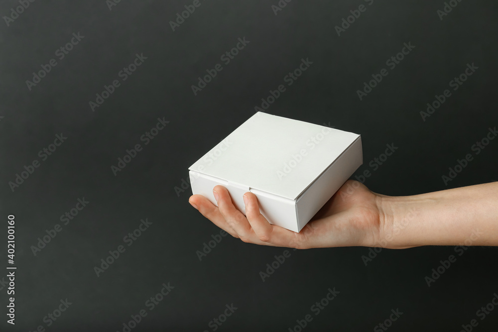 Hand with blank cardboard box on dark background