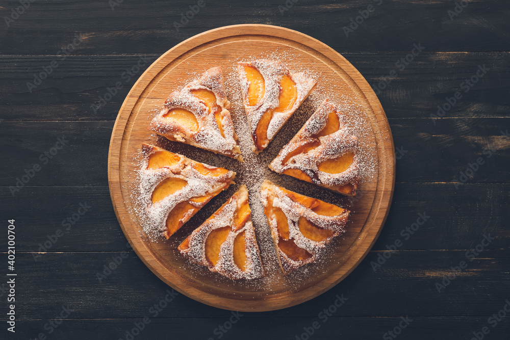 Board with tasty peach pie on dark background